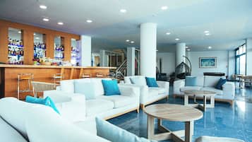 Um lobby de hotel moderno com sofás brancos, área de bar e uma escadaria.
