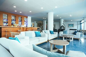 Un vestíbulo de hotel moderno con sofás blancos, una zona de bar y una escalera.