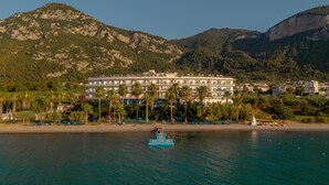 A hotel with multiple floors, a beach with sun loungers, and a boat in the water. - Sissy (Kamena Vourla)
