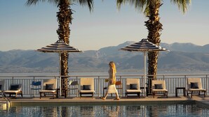 A poolside area with lounge chairs and umbrellas, overlooking a mountainous landscape. - Sissy (Kamena Vourla)