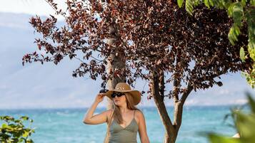 A woman walking on a pathway by the beach, with a tree and ocean in the background.