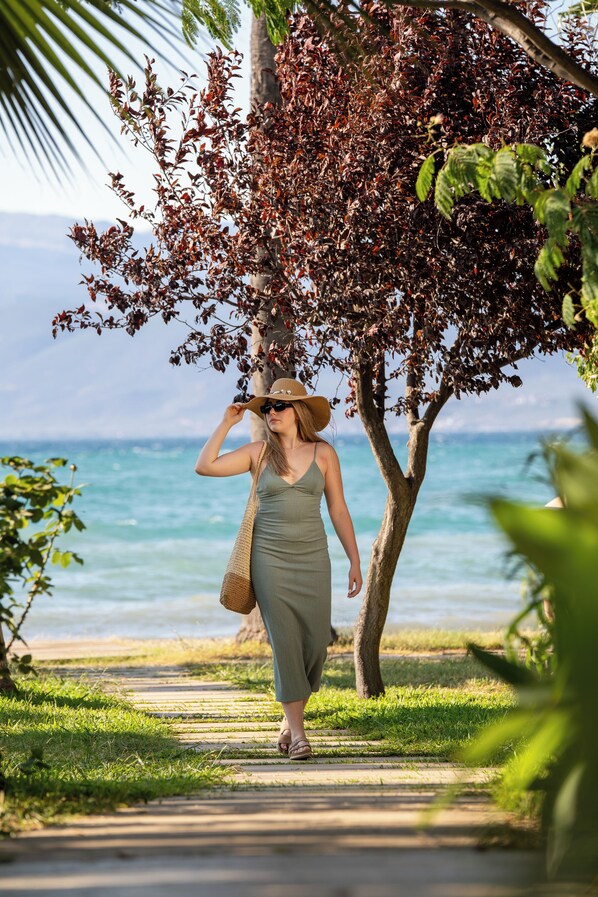 A woman walking on a pathway by the beach, with a tree and ocean in the background.