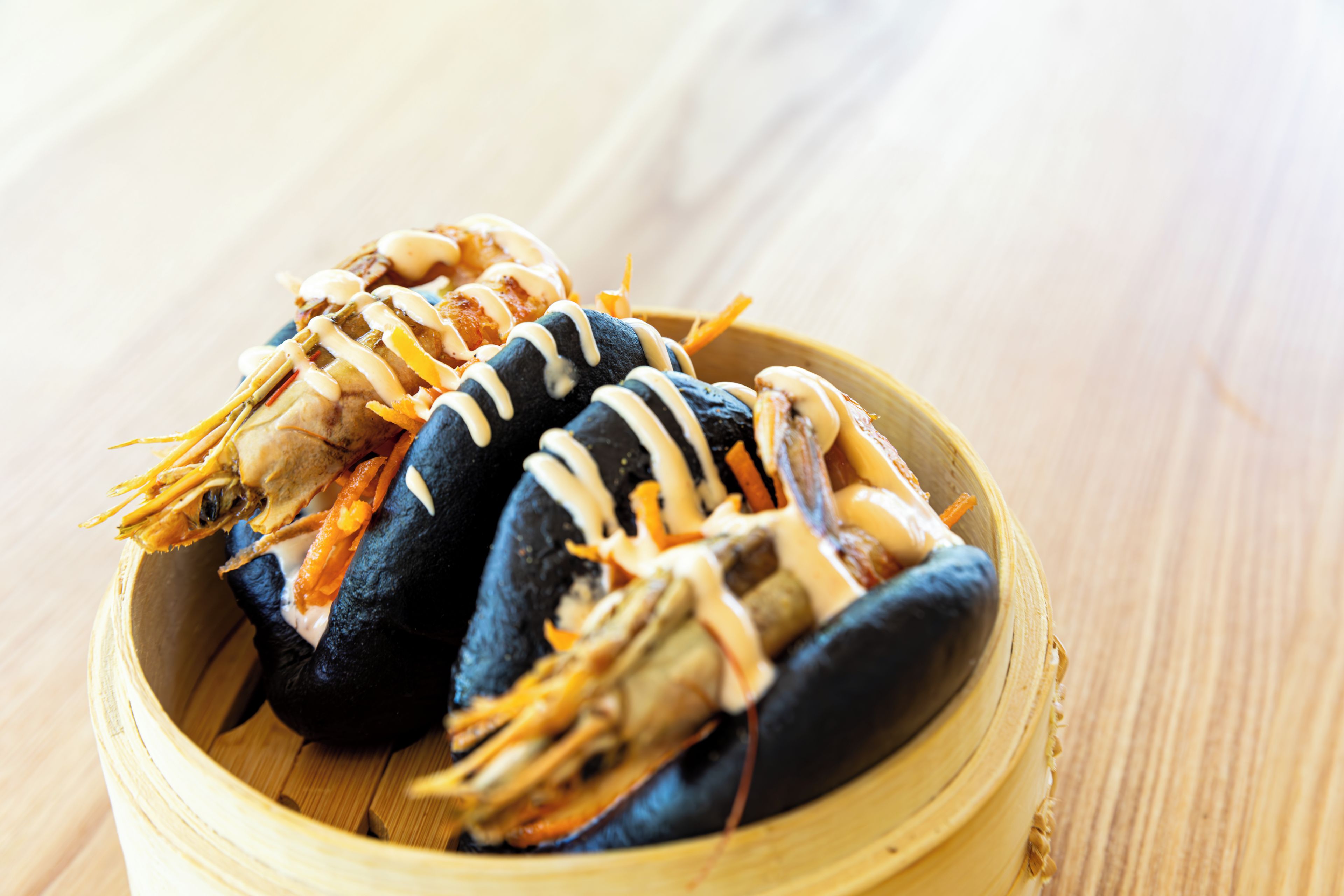 A bamboo steamer containing food items, likely dumplings or buns, with some sauce drizzled on top.