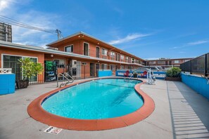 Una piscina con borde rojo, un edificio con múltiples ventanas y un cielo azul despejado.