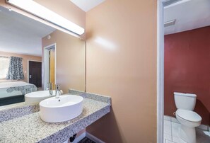 A bathroom with a white sink, a mirror, and a toilet. - Rodeway Inn Modesto (Modesto)