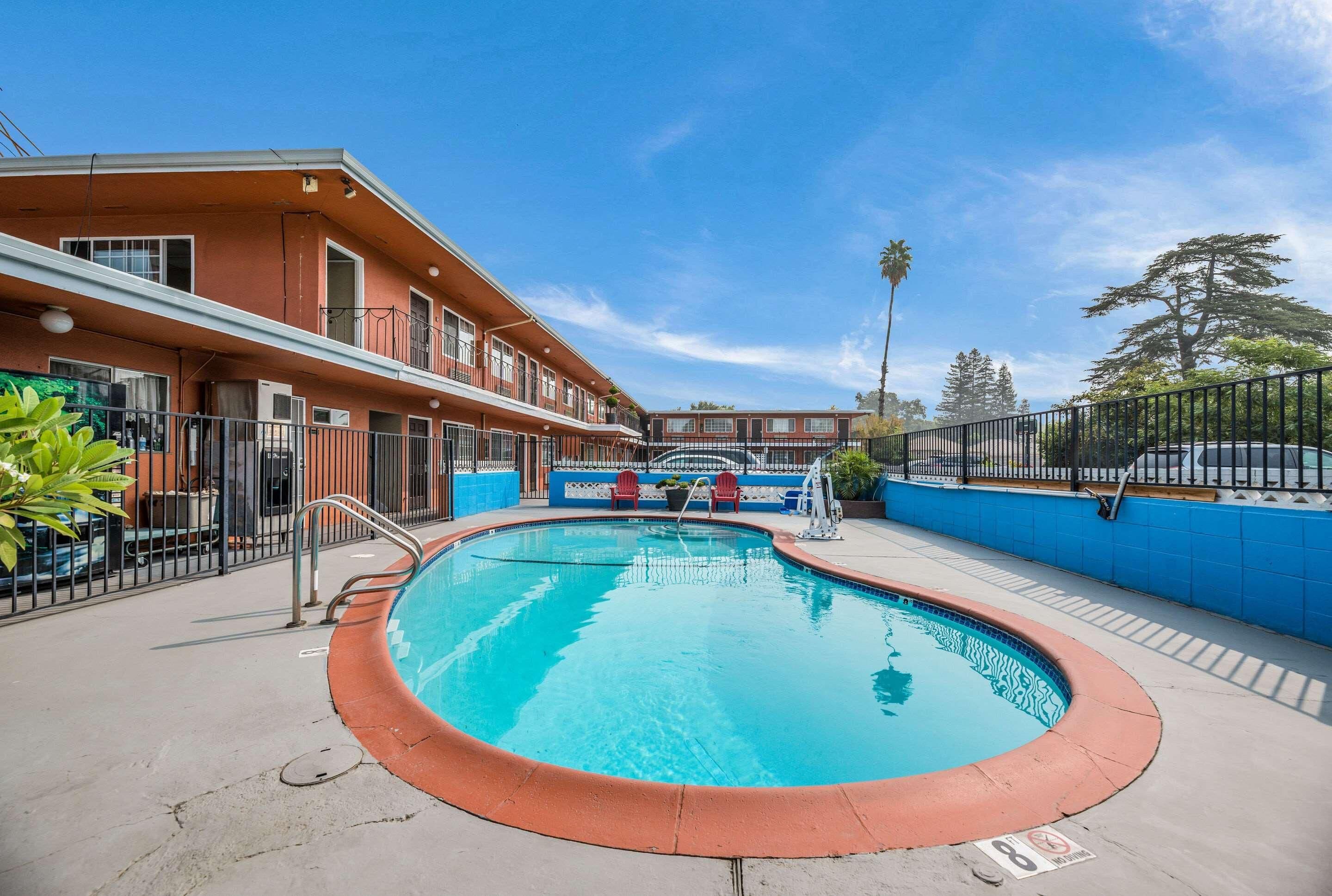 A swimming pool with a red edge, a building with balconies, and a clear blue sky.