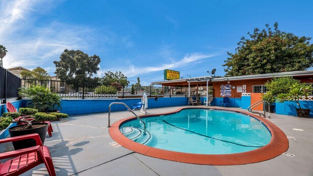 Zona de piscina con un cartel de Suburban Lodge, piscina cercada y sillas rojas.