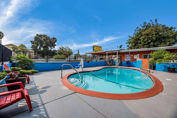A pool area with a sign for Suburban Lodge, a fenced pool, and red chairs. - Rodeway Inn Modesto (Modesto)