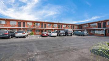 A multi-story motel with a parking lot, several cars, and a clear blue sky.