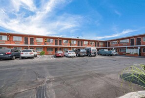 Un motel de varios pisos con un estacionamiento, varios automóviles y un cielo azul despejado.