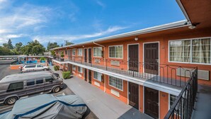 Un motel de varios pisos con fachada roja, balcones y un estacionamiento con vehículos.
