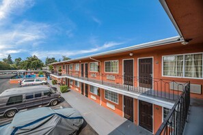 A multi-story motel with a red exterior, balconies, and a parking area with vehicles. - Rodeway Inn Modesto (Modesto)