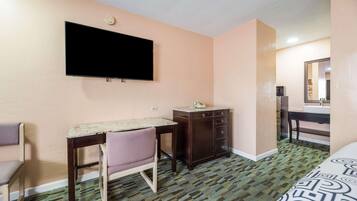 A hotel room with a bed, a desk, a chair, a dresser, a television, and a mirror.