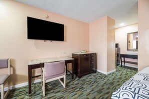 Habitación de hotel con cama, escritorio, silla, cómoda, televisor y espejo.
