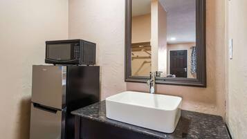 A bathroom with a white sink, a black microwave, and a refrigerator.