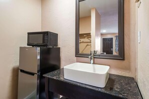Un baño con un lavamanos blanco, un microondas negro y un refrigerador.