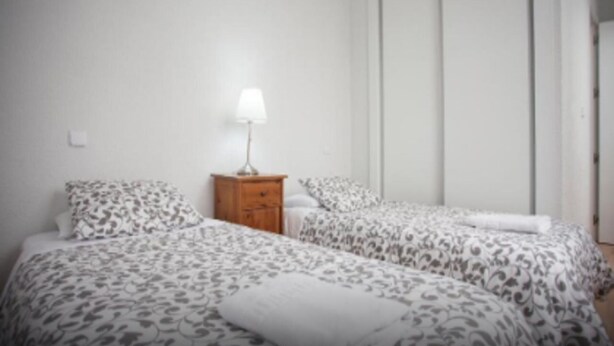 A bedroom with two beds, a nightstand with a lamp, and a wardrobe. - Apartamentos Fuencarral 50 (Madrid)