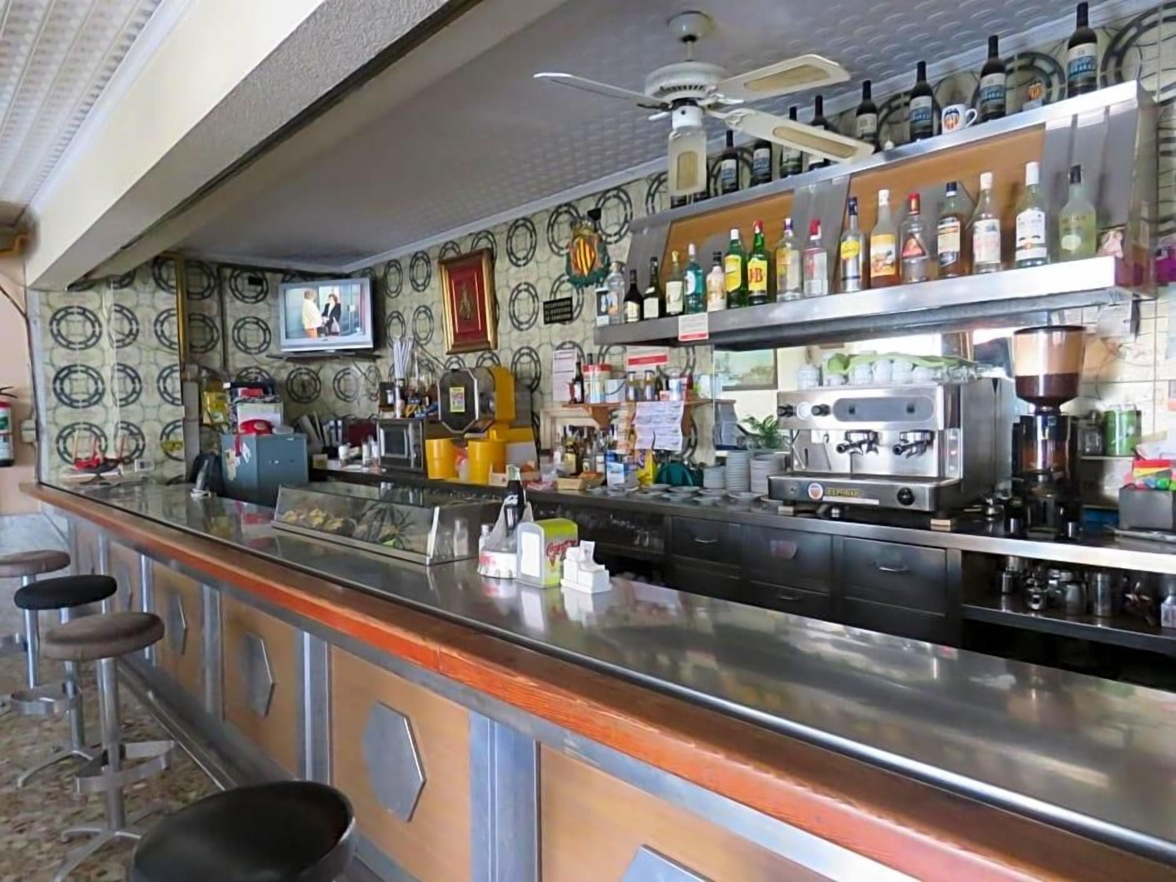 A bar area with a counter, stools, a ceiling fan, and shelves with bottles.
