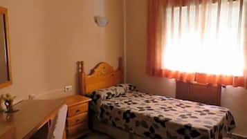 Un dormitorio con cama, escritorio, silla, ventilador de techo y ventana con cortinas.
