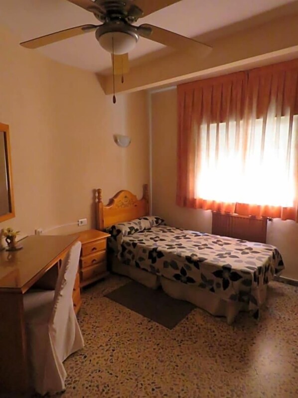 A bedroom with a bed, a desk, a chair, a ceiling fan, and a window with curtains. - Hotel Alain (Silla)