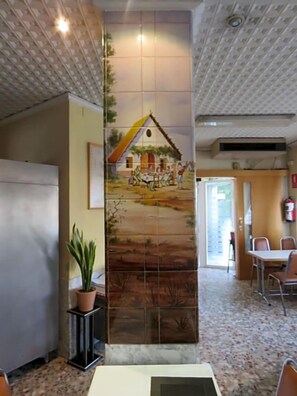A room with a tiled mural, a potted plant, a table, chairs, and a ceiling fan. - Hotel Alain (Silla)