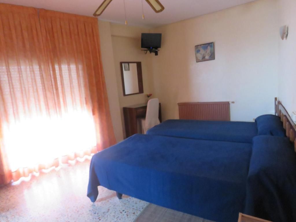 Ein Zimmer mit zwei Betten, einem an der Wand befestigten Fernseher, einem Spiegel und einem Fenster mit Vorhängen.