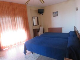 A room with two beds, a television on the wall, a mirror, and a window with curtains.