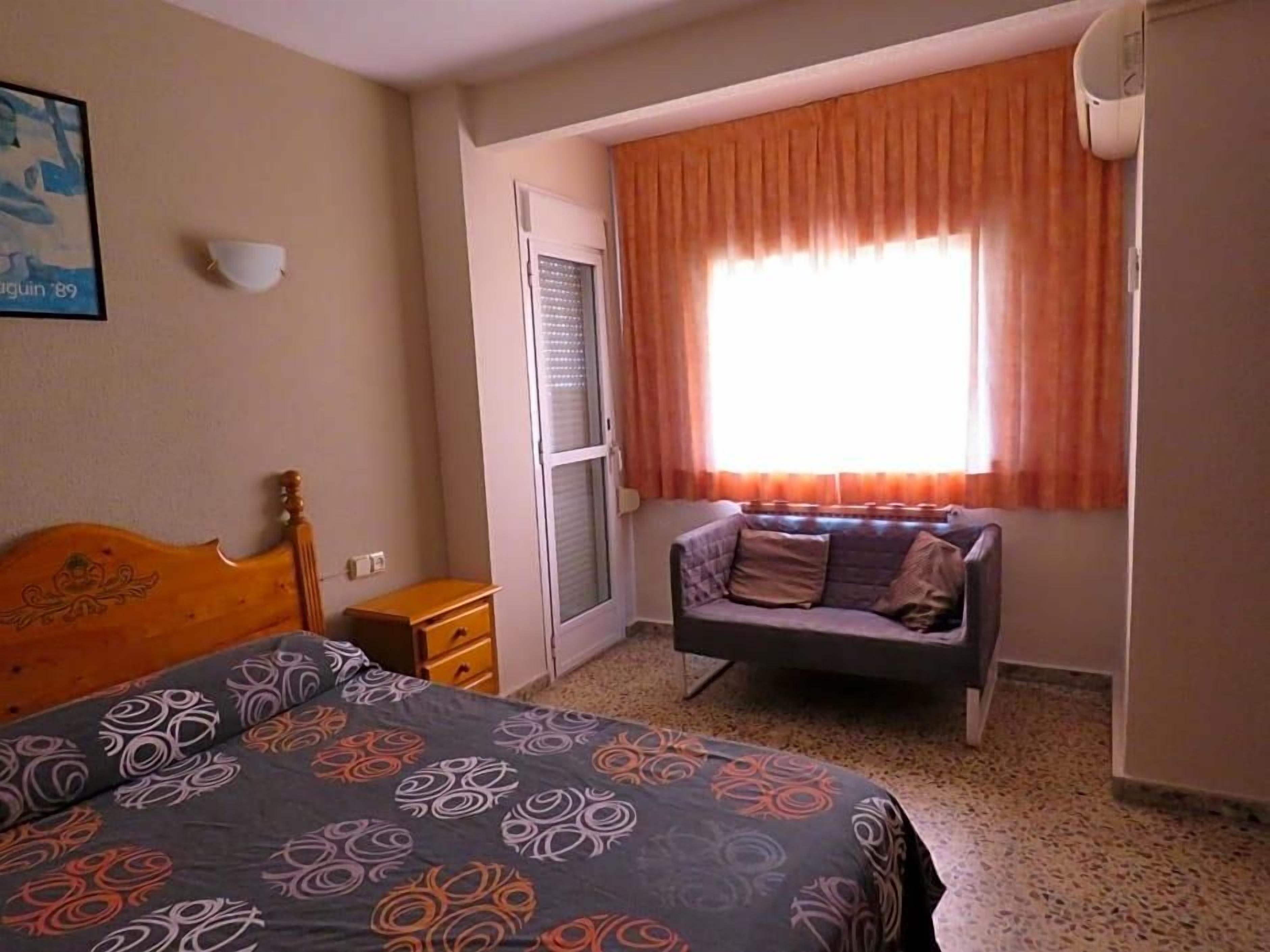Un dormitorio con cama, sofá, ventana con cortinas, lámpara de pared y puerta.