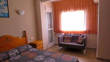 Un dormitorio con cama, sofá, ventana con cortinas, lámpara de pared y puerta.