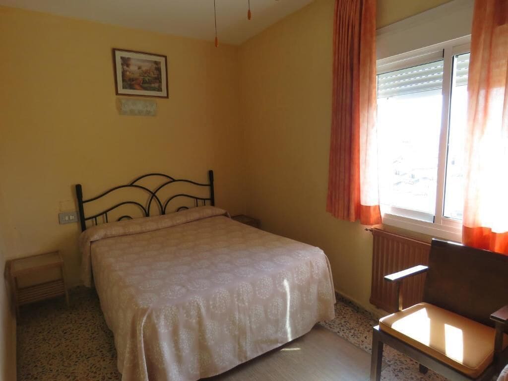 Une chambre à coucher avec un lit, une chaise, un radiateur, une fenêtre avec des rideaux et un tableau au mur.