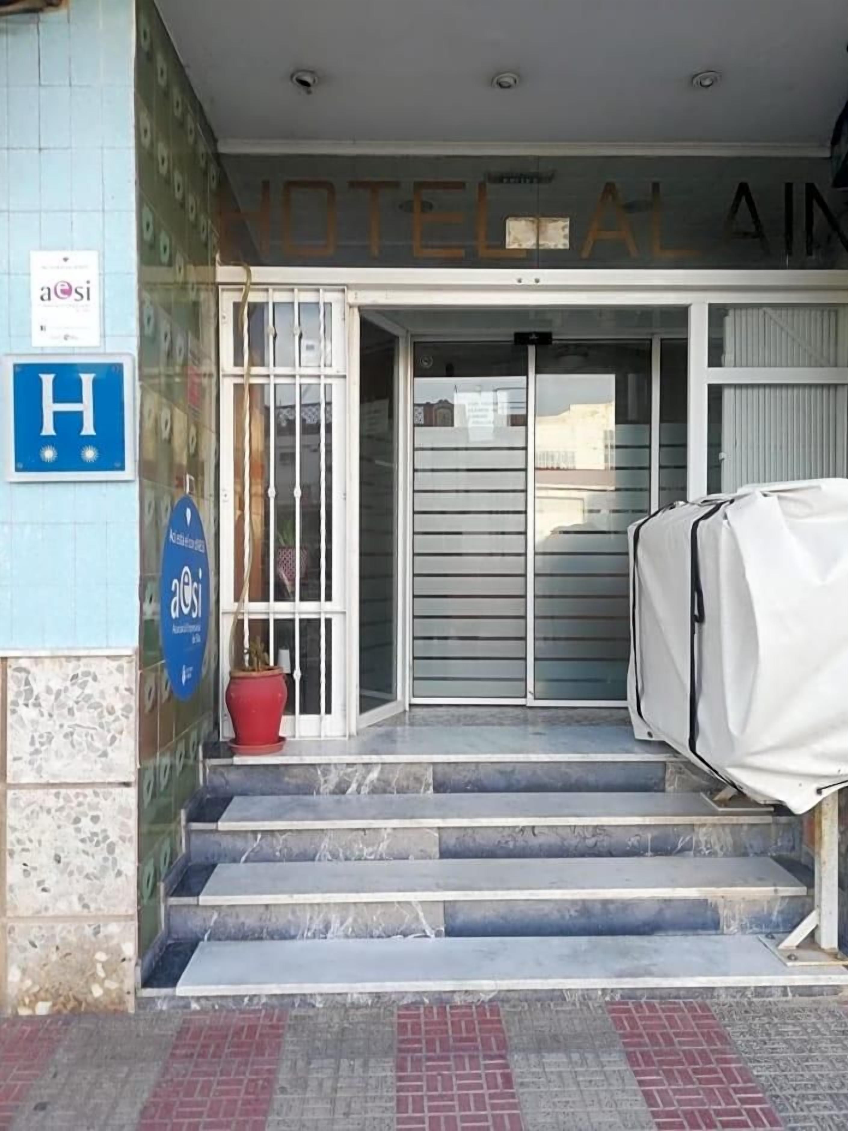 Hoteleingang mit Glastür, Topfpflanze und überdachtem Auto.