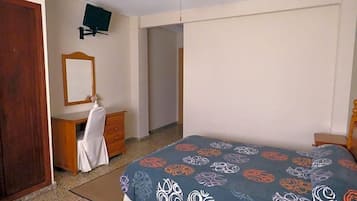 A bedroom with a bed, a dresser, a mirror, a ceiling fan, and a television on the wall.