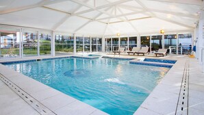An indoor swimming pool with clear glass walls, lounge chairs, and a covered roof. - Monasterio Hotel Boutique (San Carlos de Bariloche)