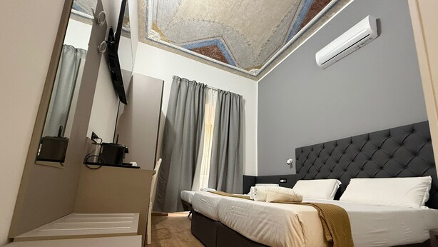 Une chambre d’hôtel moderne dotée d’un grand lit, d’un téléviseur à écran plat fixé au mur, d’un plafond orné de motifs décoratifs et d’un système de climatisation intégré.