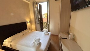 Une chambre d’hôtel avec un lit, une table de chevet, un téléviseur fixé au mur et une vue sur le balcon extérieur.