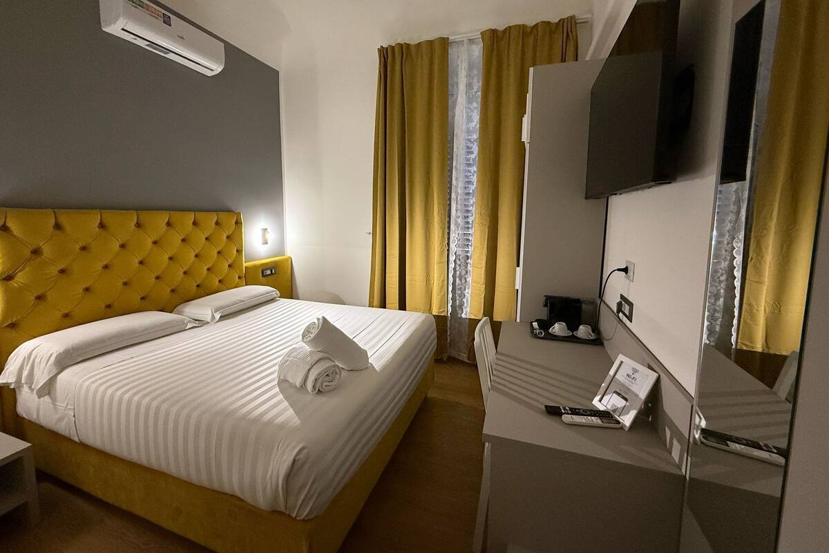 A hotel room with a bed, a bedside table, a TV, and a window with curtains.