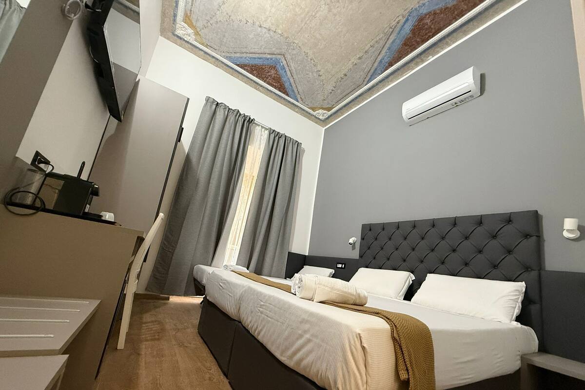 A modern hotel room with a bed, a desk, and a ceiling with a geometric design.