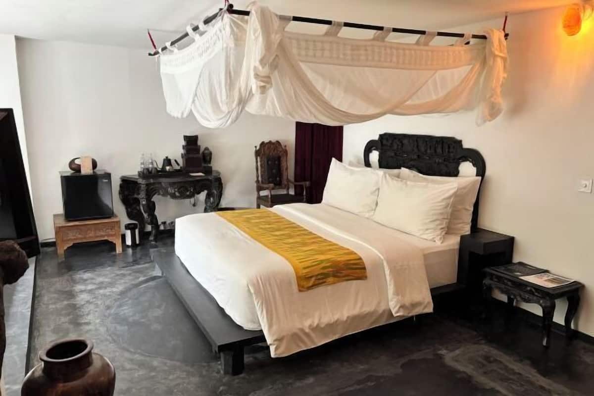 A bedroom with a bed, bedside tables, a nightstand, a decorative vase, and a canopy.
