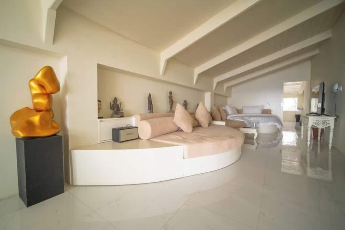 A modern bedroom with a curved bed, a decorative sculpture, and a small table.