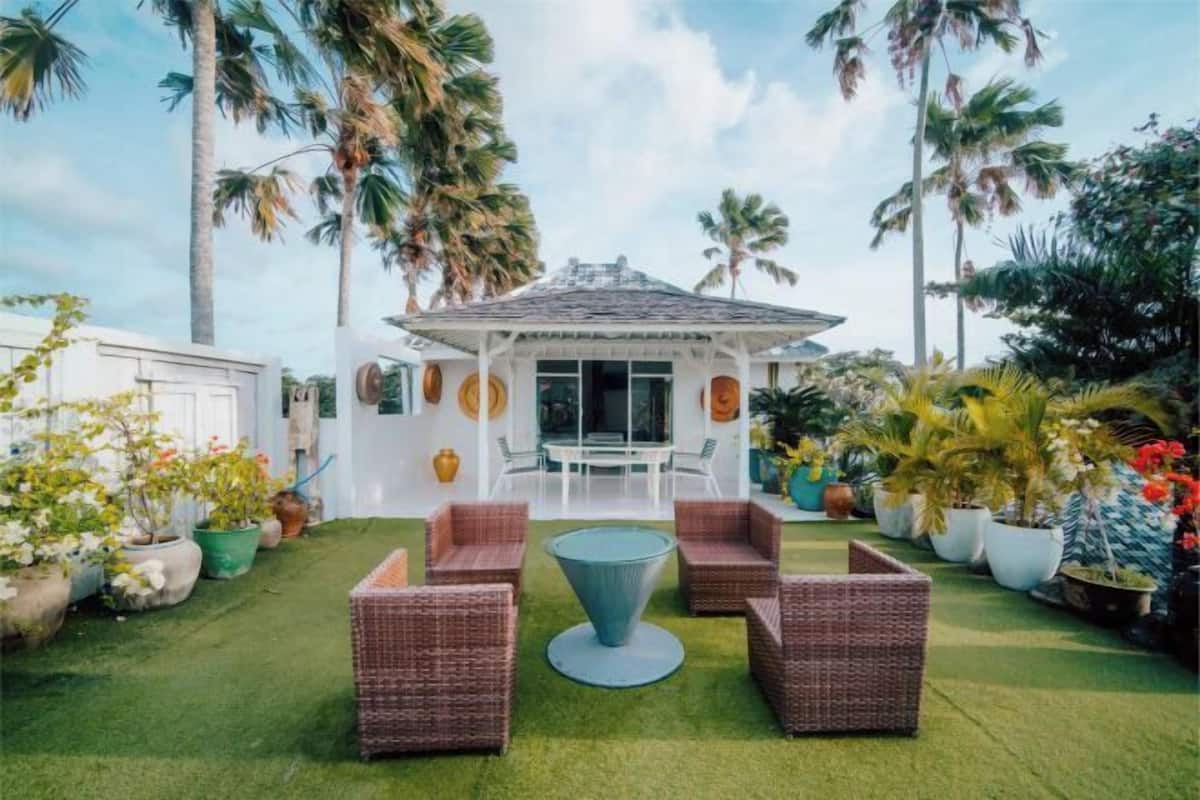A patio with wicker furniture, a round table, and a white building with a tiled roof.