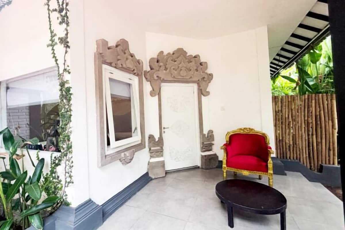 A room with a red chair, a small table, a door with decorative moldings, and a window.