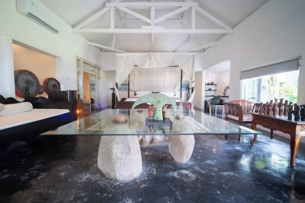 A spacious room with a glass coffee table, a bed, and a dining area with chairs.