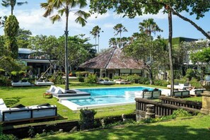 A swimming pool with lounge chairs, a thatched-roof structure, and palm trees. - Morabito Art Villa (Canggu)