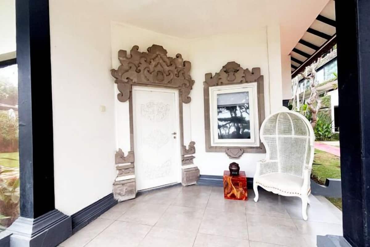 A room with a white door, a framed picture, a white wicker chair, and a small table with a decorative item.