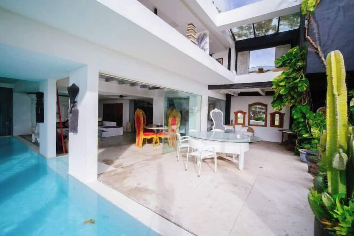A modern house with a glass-enclosed patio, a pool, and a cactus plant.
