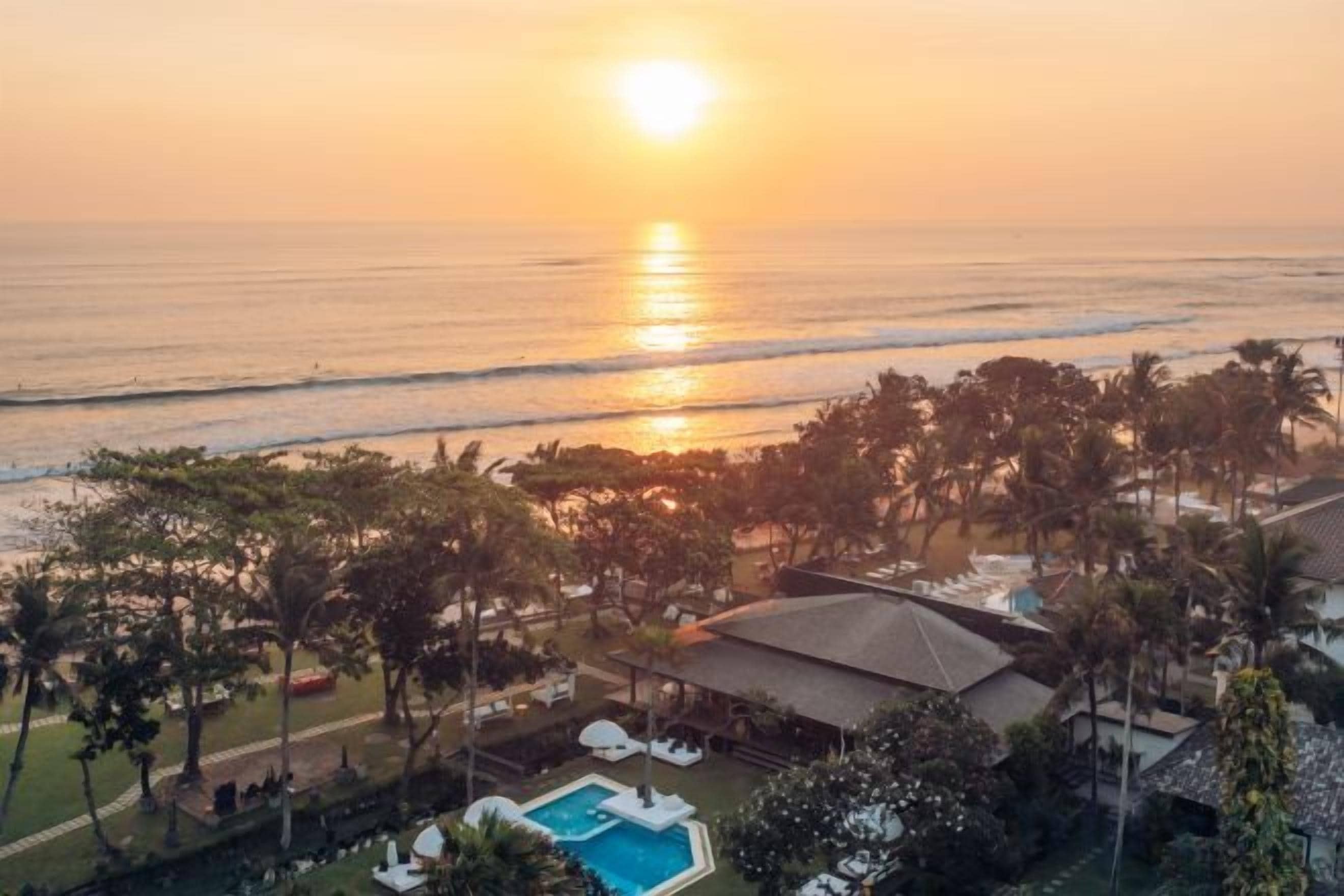 A resort with a pool, beach view, and palm trees.