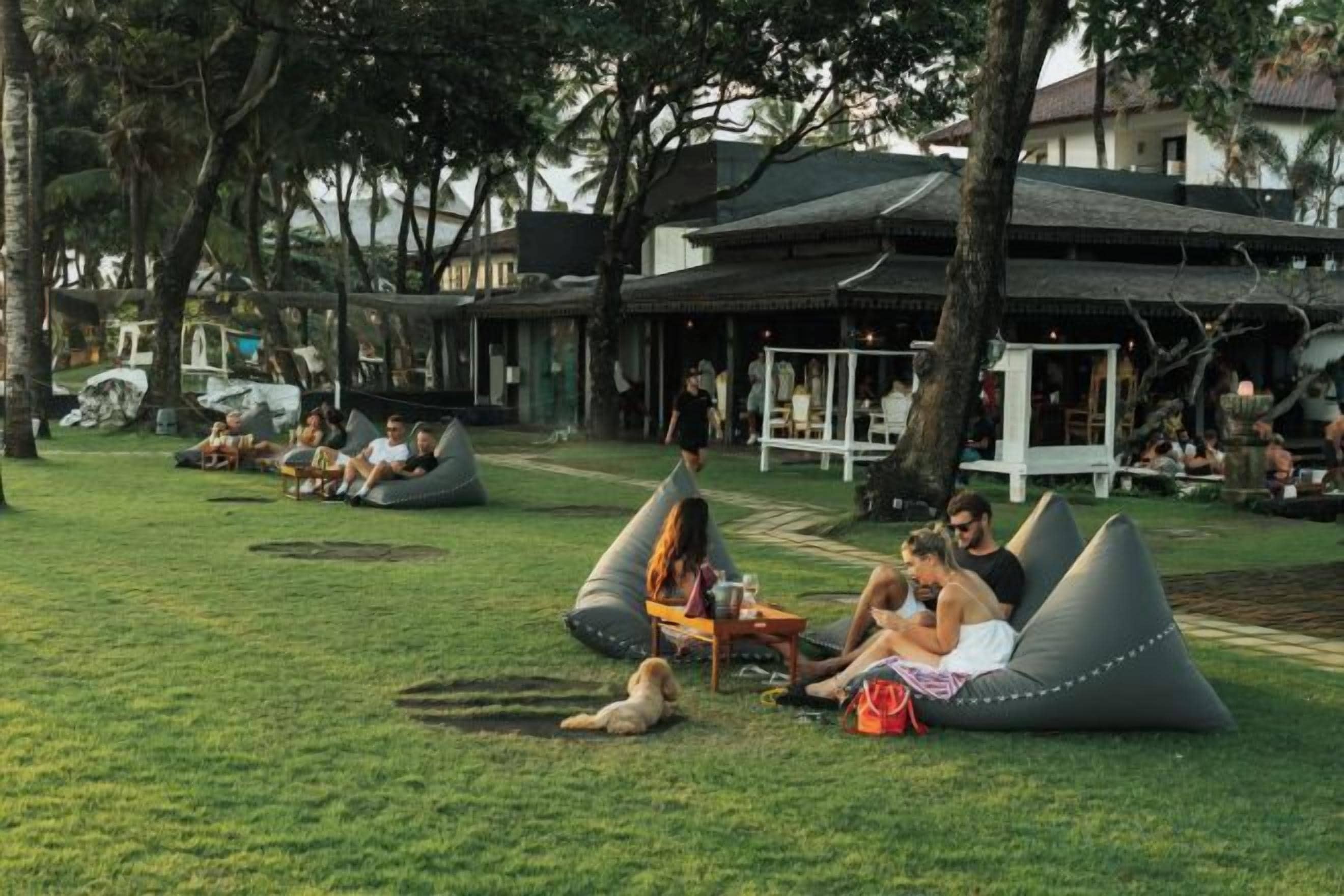 An outdoor seating area with bean bags and a grassy lawn, surrounded by trees and a building with a covered patio.