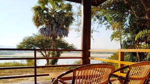 A wooden deck with wicker chairs overlooking a river and distant mountains. - Bagan Village Resort Hotel (Nyaung-U)
