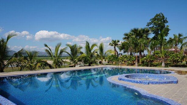 A swimming pool with blue tiles, surrounded by palm trees and greenery. - Bagan Village Resort Hotel (Nyaung-U)