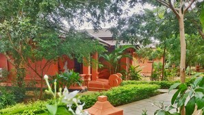 A courtyard with a red brick building, surrounded by lush greenery and a paved walkway. - Bagan Village Resort Hotel (Nyaung-U)